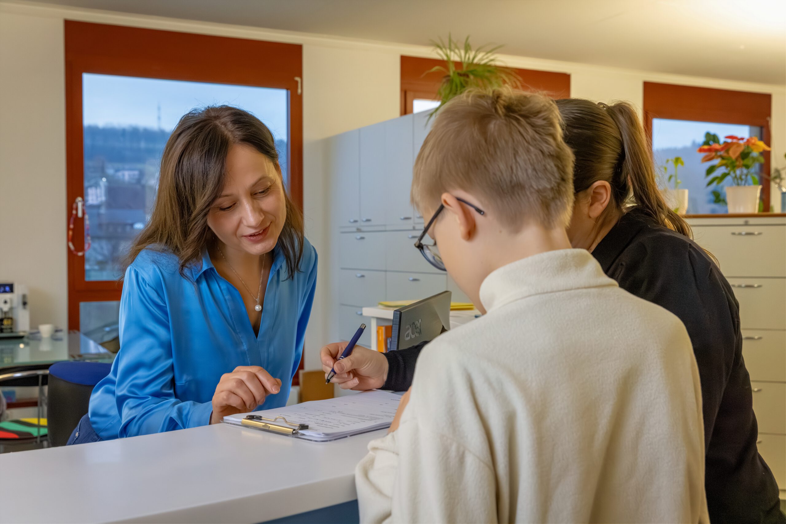 Eine Sekretärin hilft einer Mutter mit einem Jungen beim Ausfüllen eines Formulars