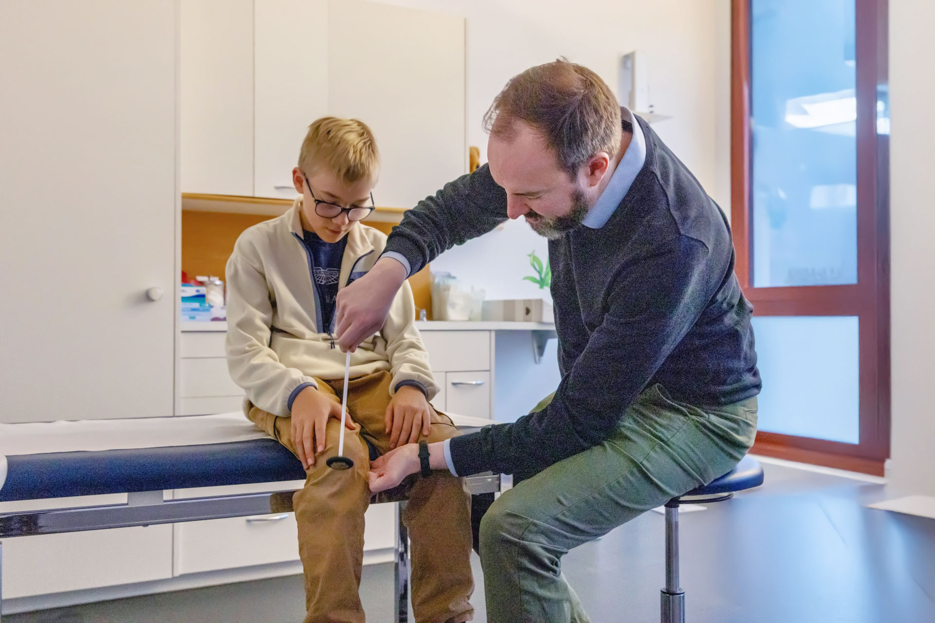 Ein Arzt prüft den Knie-Reflex eines Jungen